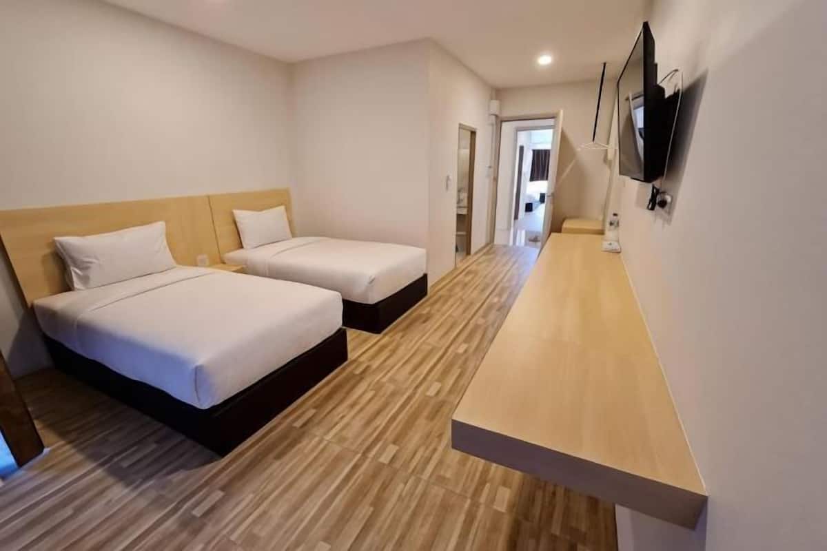 Een hotelkamer met twee bedden, een houten vloer, een aan de muur bevestigde televisie en een houten bankje.