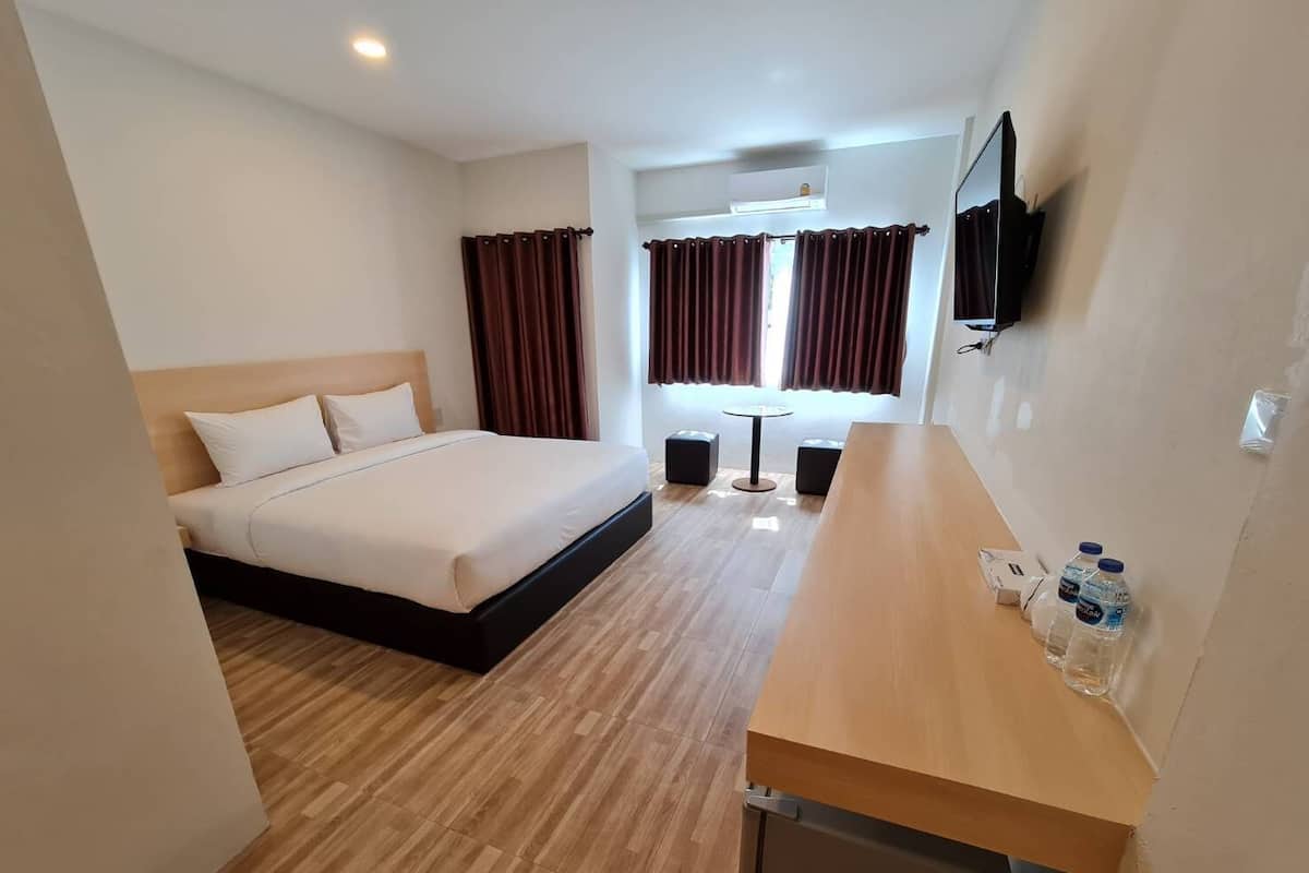 Een hotelkamer met een bed, een houten bureau, een televisie en een raam met gordijnen.