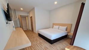 Een moderne hotelkamer met een houten vloer, een bed met witte lakens, een nachtkastje en een aan de muur bevestigde televisie.
