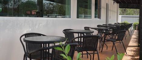 An outdoor patio with black wicker chairs and round tables, large windows, and a view of the surrounding area.
