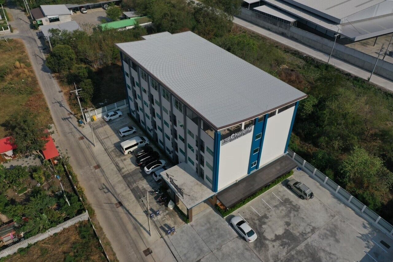 A multi-story building with a flat roof, a parking lot, and a small adjacent structure with a sign.