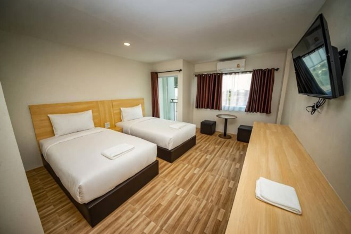 Ett hotellrum med två sängar, ett skrivbord i trä, en TV och ett fönster med gardiner.