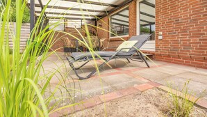 A patio with a lounge chair, a wicker table, and a brick wall. - Ferienhaus "bräist Hus" in Bredstedt für bis zu 5 Personen (Bredstedt)