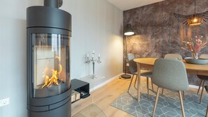 A modern interior with a wood-burning stove, dining table, chairs, and a patterned wall. - Ferienhaus "bräist Hus" in Bredstedt für bis zu 5 Personen (Bredstedt)