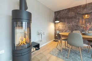 A modern interior with a wood-burning stove, dining table, chairs, and a patterned wall. - Ferienhaus "bräist Hus" in Bredstedt für bis zu 5 Personen (Bredstedt)