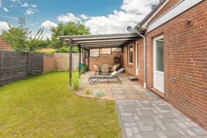 Un jardin avec une terrasse, un mur en briques, une clôture en bois et un potager.