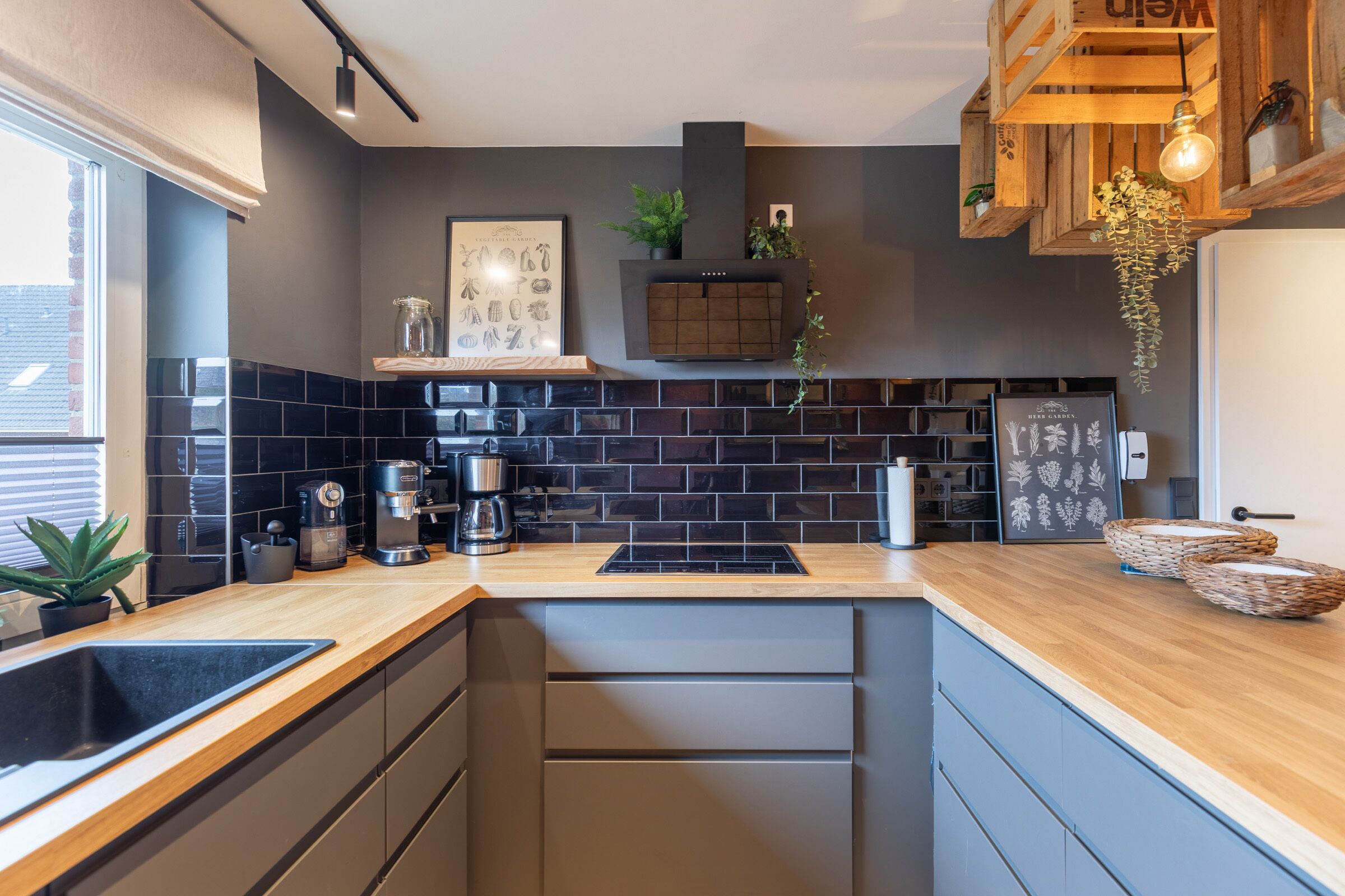 Une cuisine moderne avec un dosseret de carreaux noirs, des plans de travail en bois, une cuisinière encastrée et une machine à café.