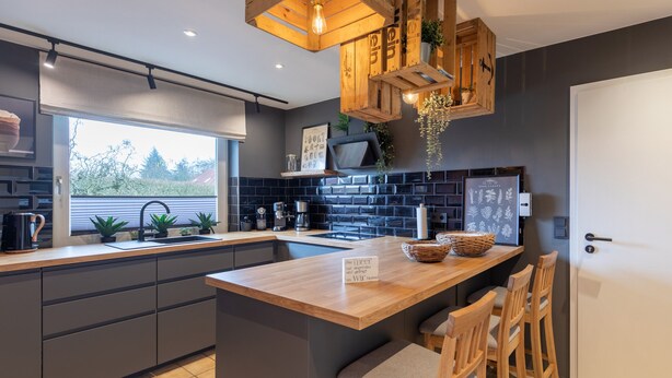 A modern kitchen with a central island, dark backsplash, and wooden accents. - Ferienhaus "bräist Hus" in Bredstedt für bis zu 5 Personen (Bredstedt)