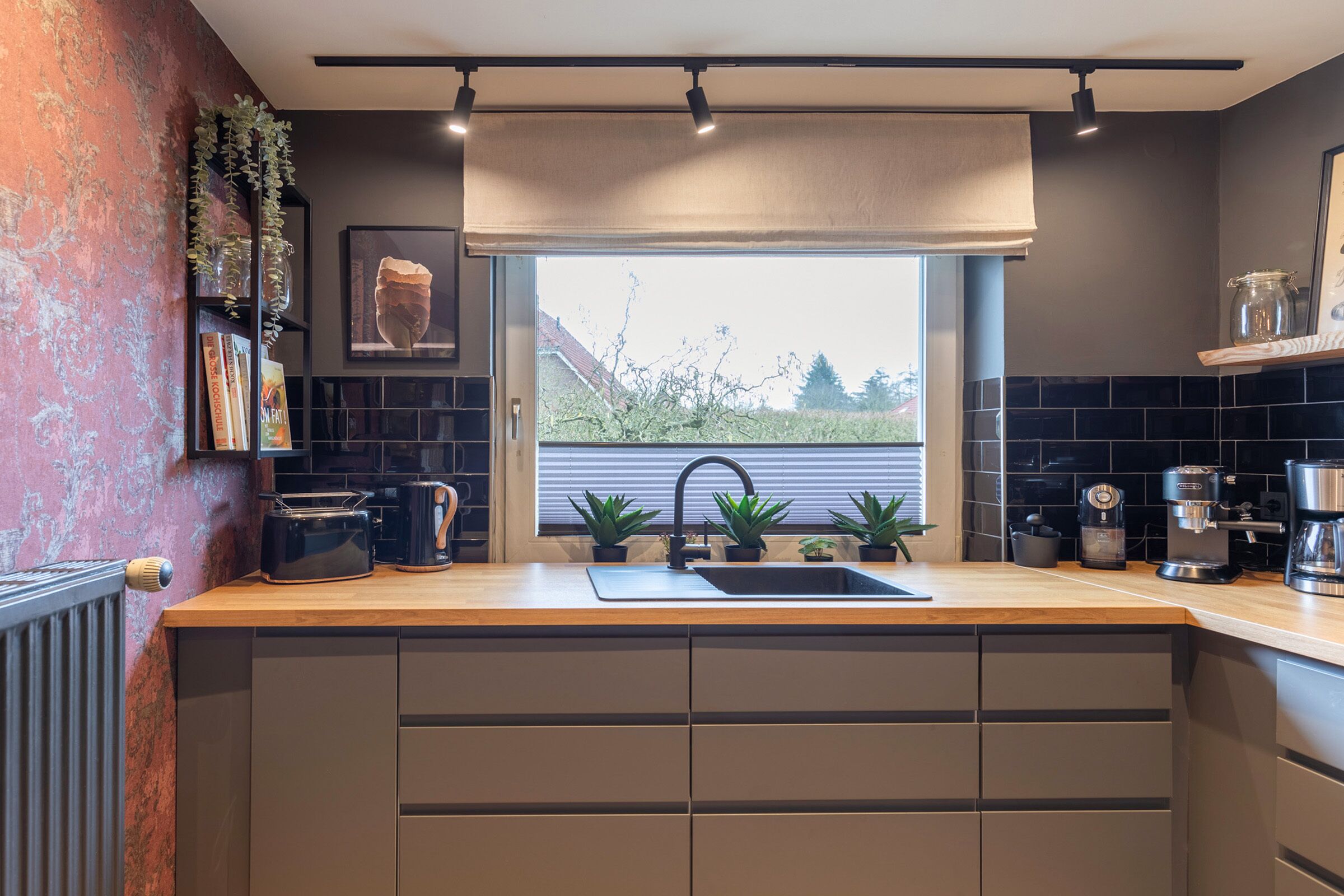 Una cocina moderna con encimera de madera, pileta negra y ventana con vistas a zonas verdes.