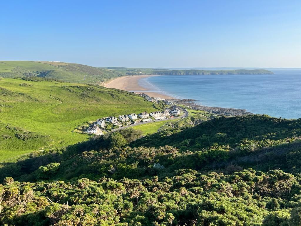 Un paysage côtier comprenant une plage, des collines douces et un ensemble de bâtiments.