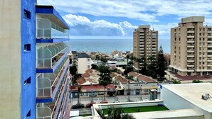 Un paisaje urbano costero con un edificio azul destacado que tiene balcones, junto a una playa.