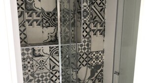 Una ducha con puerta de vidrio y pared de azulejos decorativos.