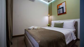 Una habitación de hotel con cama, mesita de noche, lámpara y aire acondicionado instalado en la pared.