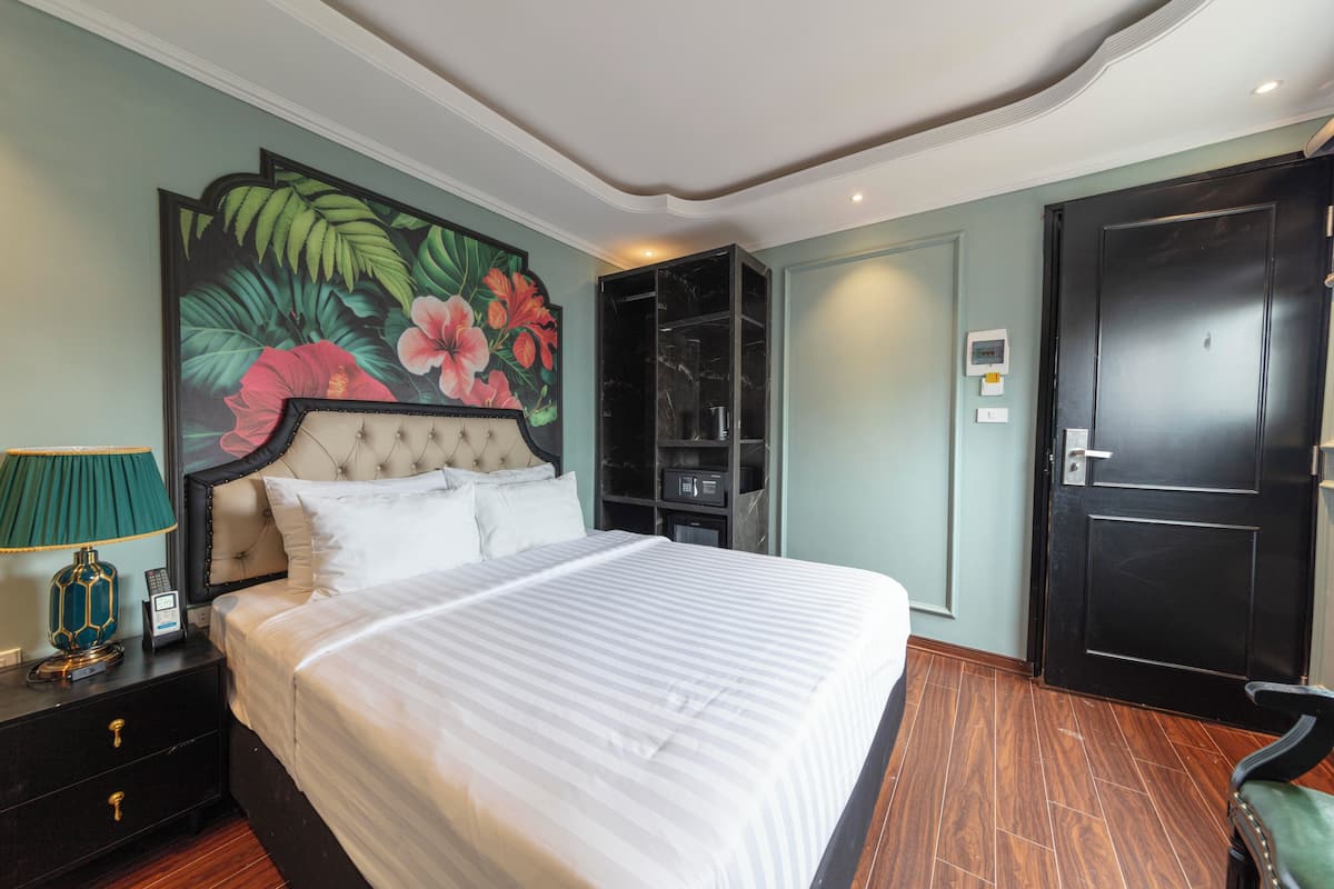 A neatly arranged bedroom with a large bed, a nightstand with a lamp, a wardrobe, and a door.