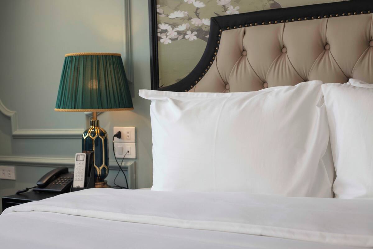 A neatly made bed with white linens, a green lamp, and a telephone on a bedside table.
