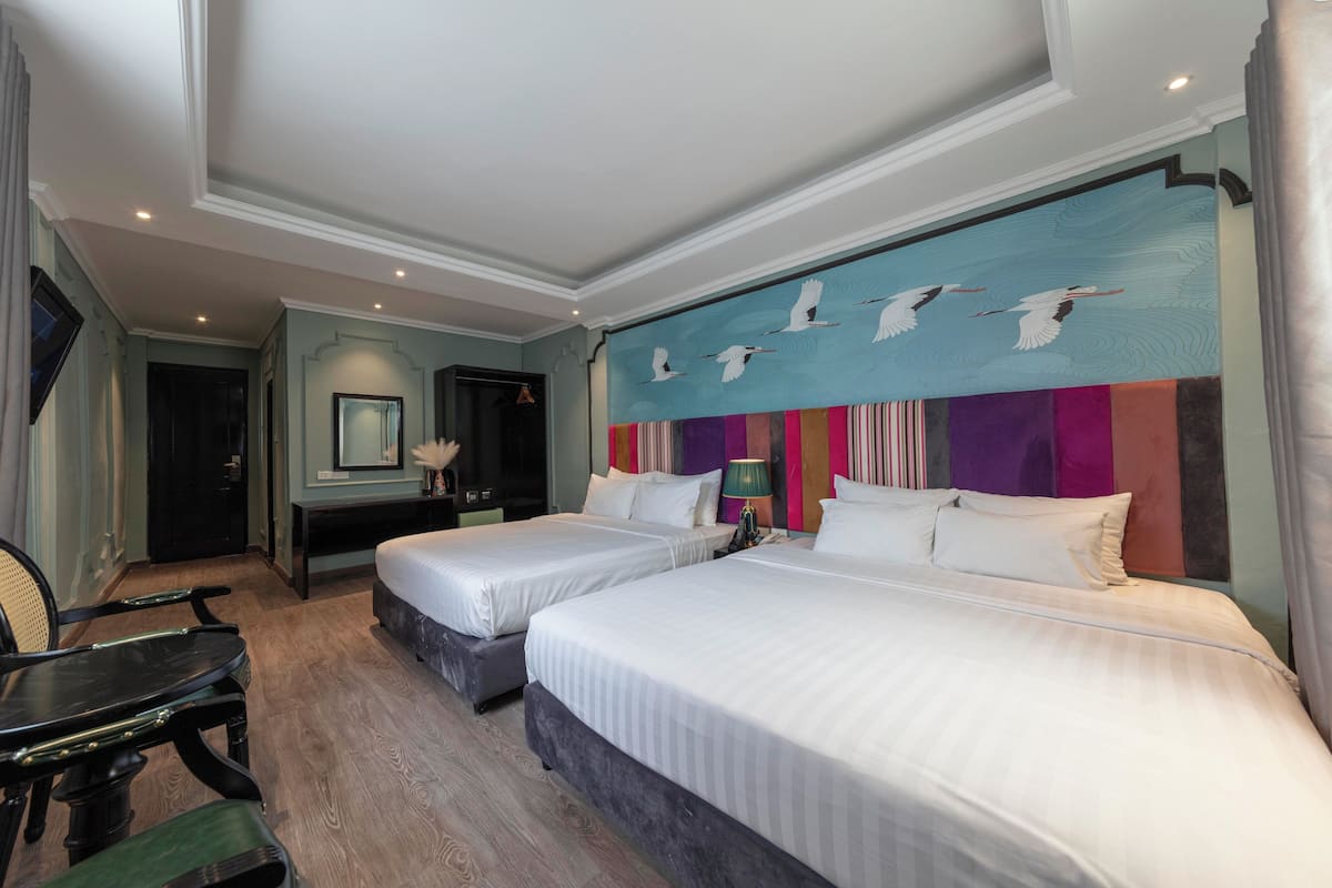 A hotel room with two beds, a desk, a chair, and a large wall mural.