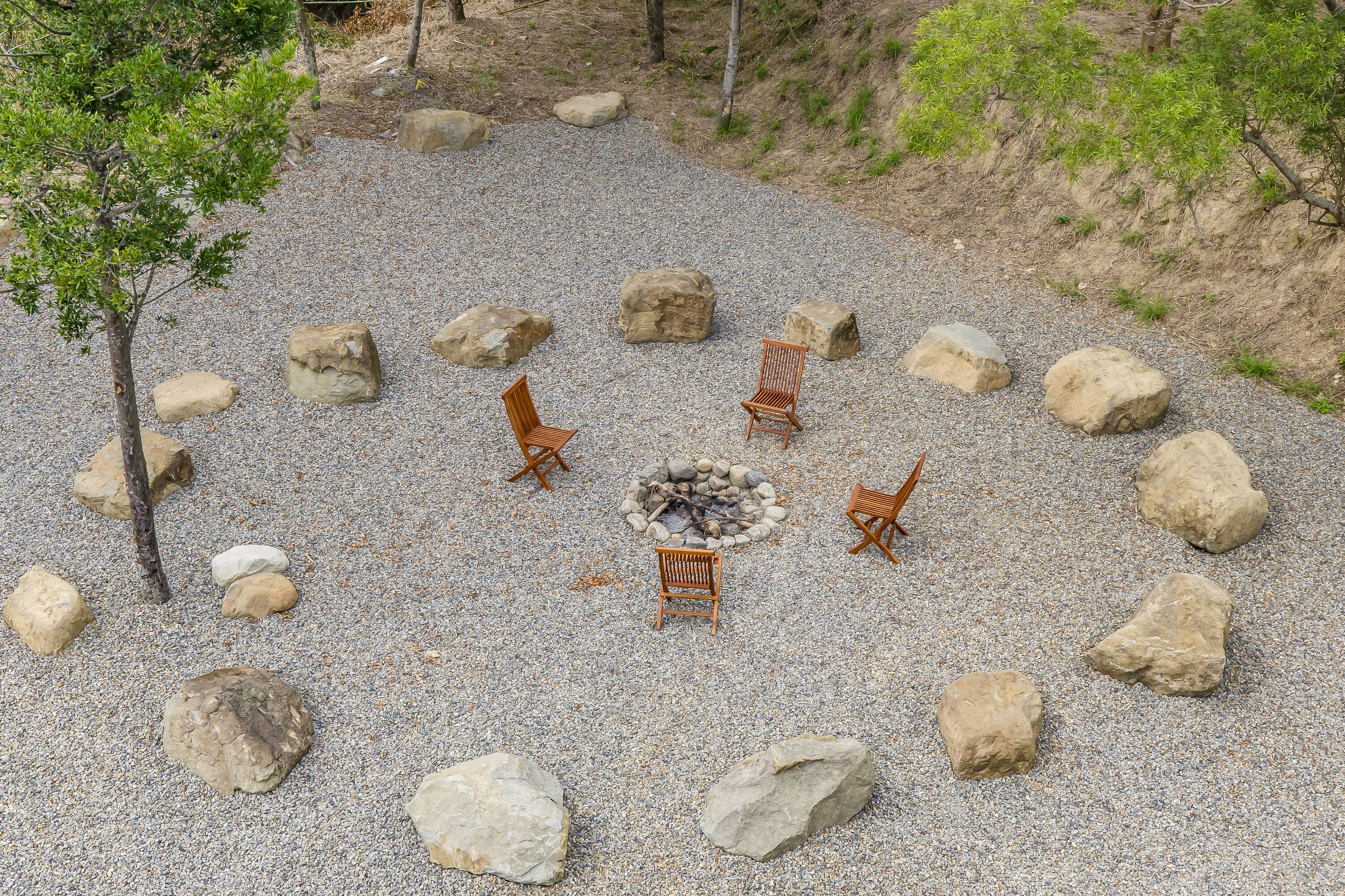 A circular seating area with a fire pit surrounded by large rocks and wooden chairs.