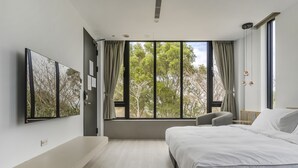 Un dormitorio moderno con una cama grande, un televisor de pantalla plana y vistas a árboles por la ventana.