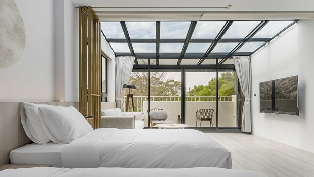 Una habitación de hotel moderna con una cama grande, una zona de estar con mesa y sillas, y un balcón con puerta de cristal.