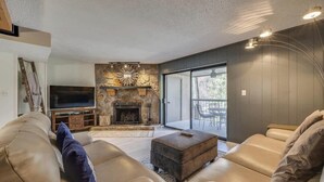 A modern living room with a stone fireplace, leather sofas, a flat-screen TV, and a large sliding glass door to a balcony.