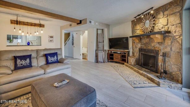 A modern living room with a stone fireplace, a sofa with decorative pillows, a television, and a remote control on a coffee table.