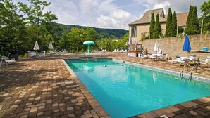 A rectangular swimming pool with a tiled deck, surrounded by lounge chairs and umbrellas.