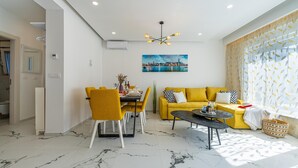 Un salon moderne comprenant un coin repas, un ensemble de canapés jaunes et un tableau représentant un paysage urbain accroché au mur.