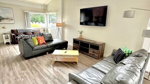 Un salon spacieux comprenant un grand canapé, un petit divan, une table basse et un téléviseur fixé au mur.