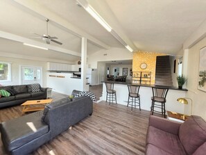 Una sala moderna con sofá, reposapiés y un comedor con taburetes de bar.