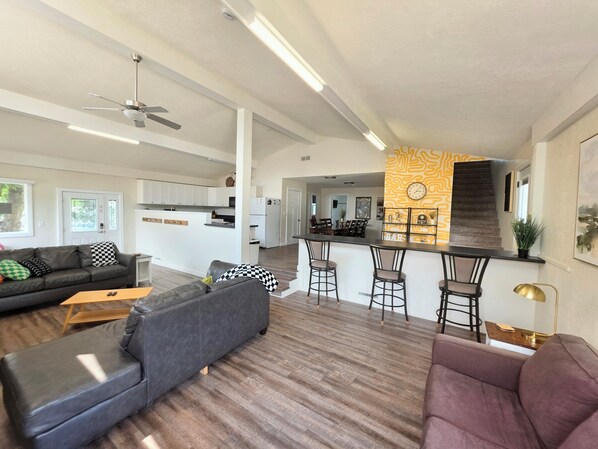 A modern living room with a sofa, ottoman, and a dining area with bar stools.