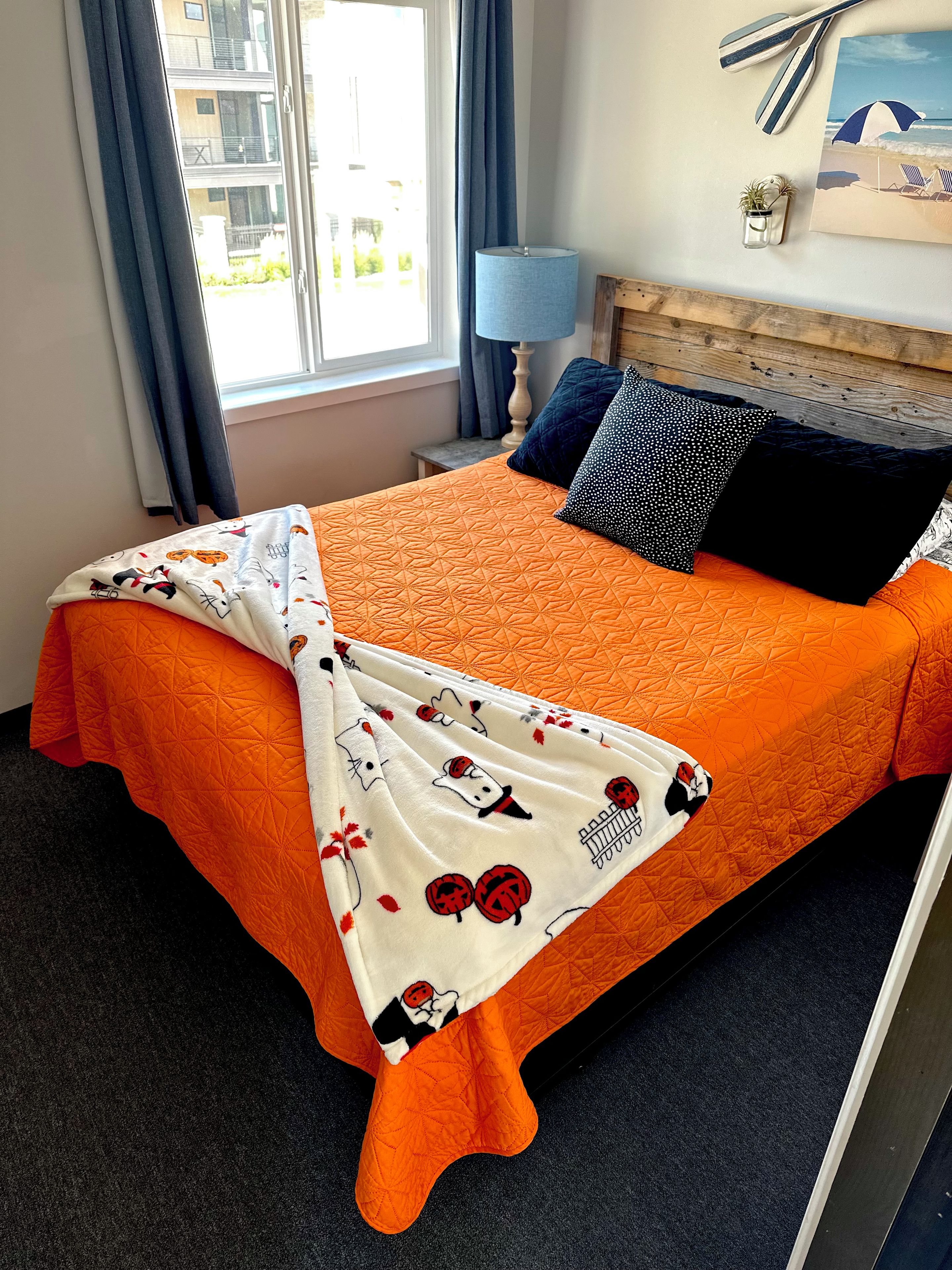 Une chambre d’hôtel avec un lit, une fenêtre avec des rideaux, une lampe, une petite table et un élément de décoration murale.