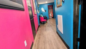 A hallway with a wooden floor, a pink wall, and a blue wall with a mirror and framed pictures.