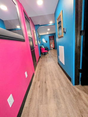 A hallway with a wooden floor, a pink wall, and a blue wall with a mirror and framed pictures. - Suite for 9 Guests in Arnolds Park (Arnolds Park)