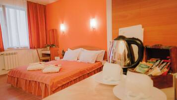 Una habitación de hotel con cama, una mesa con hervidor y un mueble para revistas.