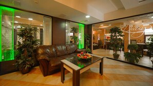 A lobby with a leather sofa, a glass coffee table with fruit, and potted plants. - Flora Residence Daisy (Samokov)