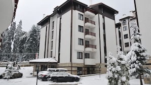 A multi-story hotel with balconies, a parking area, and snow-covered trees. - Flora Residence Daisy (Samokov)