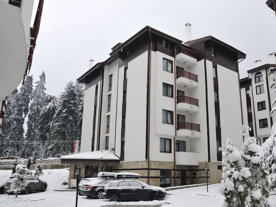 Un hotel de varios pisos con balcones, un estacionamiento y árboles cubiertos de nieve.