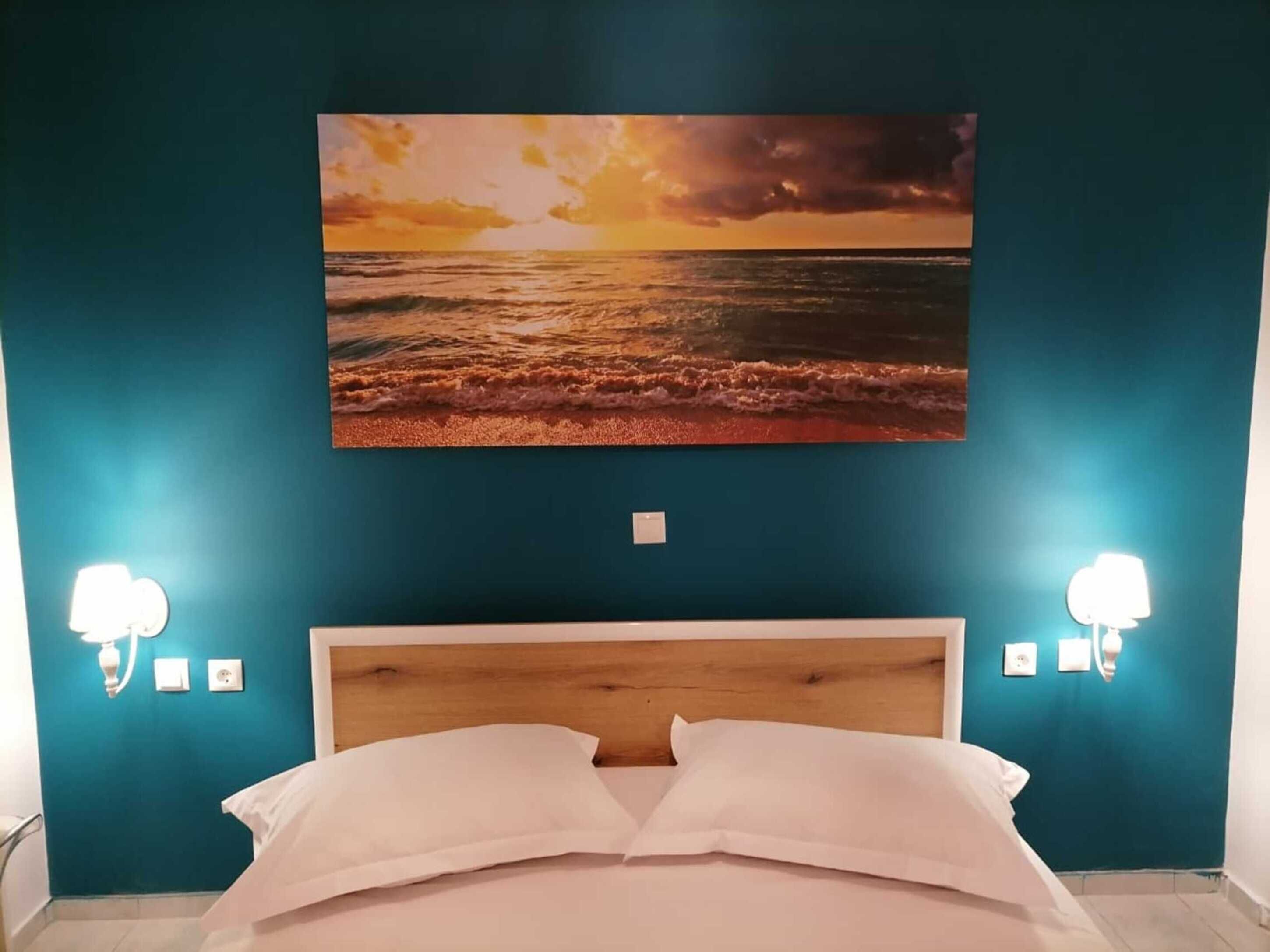 A bedroom with a wooden headboard, a bed with white linens, and a sunset beach painting on the wall.