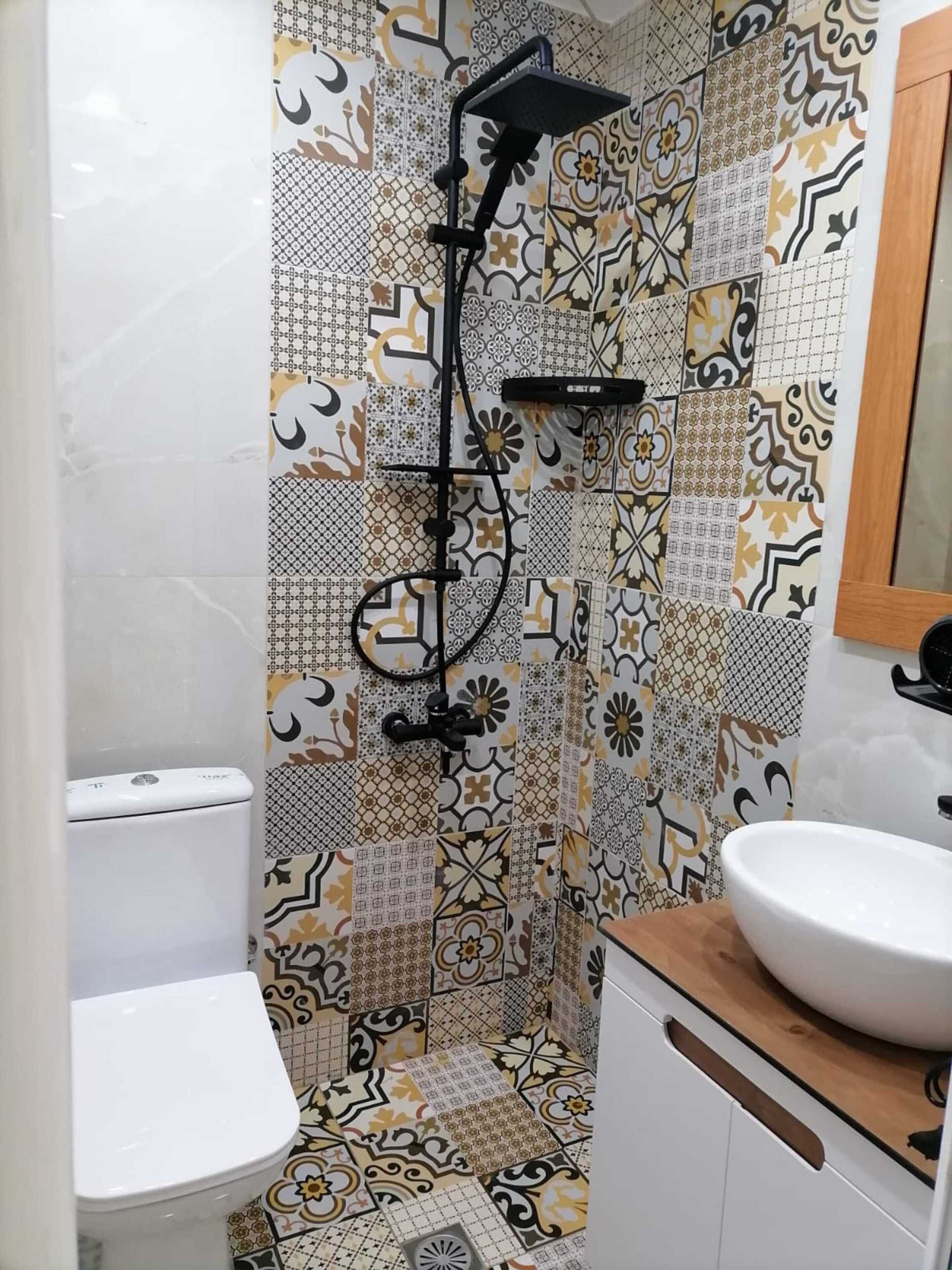 Une salle de bain avec des toilettes blanches, un lavabo doté d’un plan de travail en bois et une douche avec un tuyau noir.