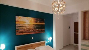 Quarto com cama, pintura do pôr do sol, lustre e banheiro com cortinas listradas.