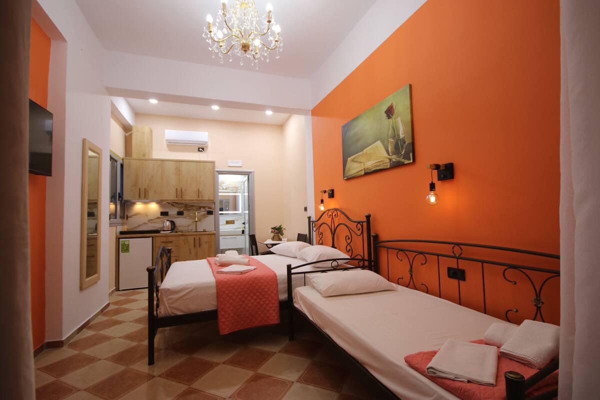 A compact room with two single beds, a kitchenette, and a dining area.