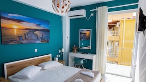 Quarto de hotel com uma cama, uma escrivaninha, uma cadeira, uma varanda e uma pintura de um pôr do sol.
