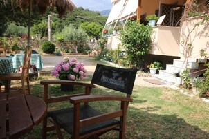 Una silla de madera con cojín negro y respaldo con la marca POWERADE, ubicada en un jardín con muro de piedra, plantas en macetas y un edificio al fondo.