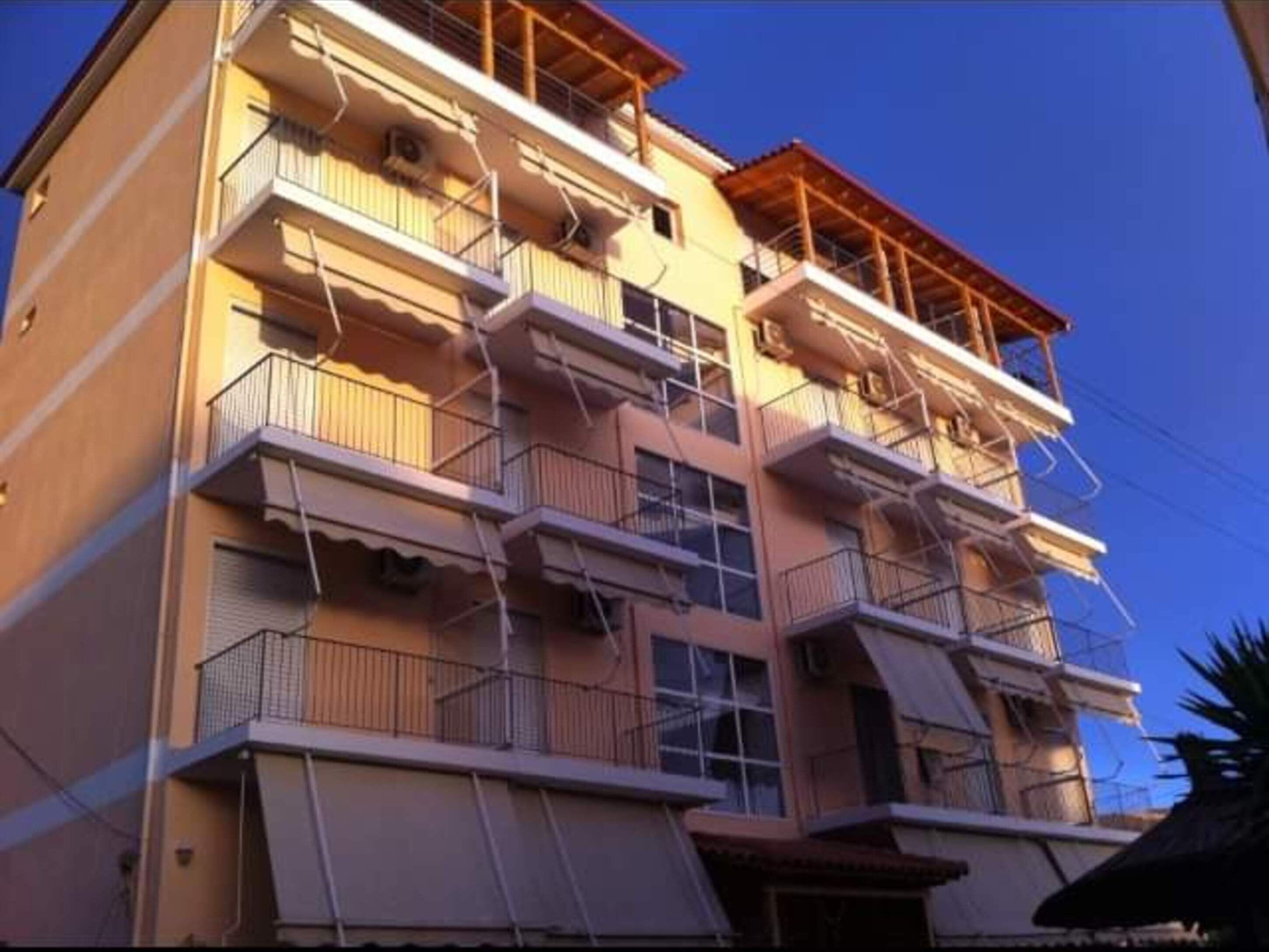 A multi-story building with balconies, a wooden facade, and a clear sky.