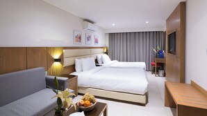 Une chambre d’hôtel comprenant un lit, un canapé, une table de chevet avec un panier de fruits, une télévision et un meuble de rangement.