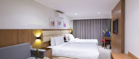 A hotel room with a bed, a sofa, a bedside table with a fruit bowl, a TV, and a cabinet.