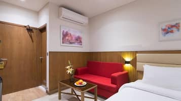 Habitación de hotel con puerta de madera, sofá rojo, una mesita con un florero y fruta, una cama y dos aires acondicionados instalados en la pared.