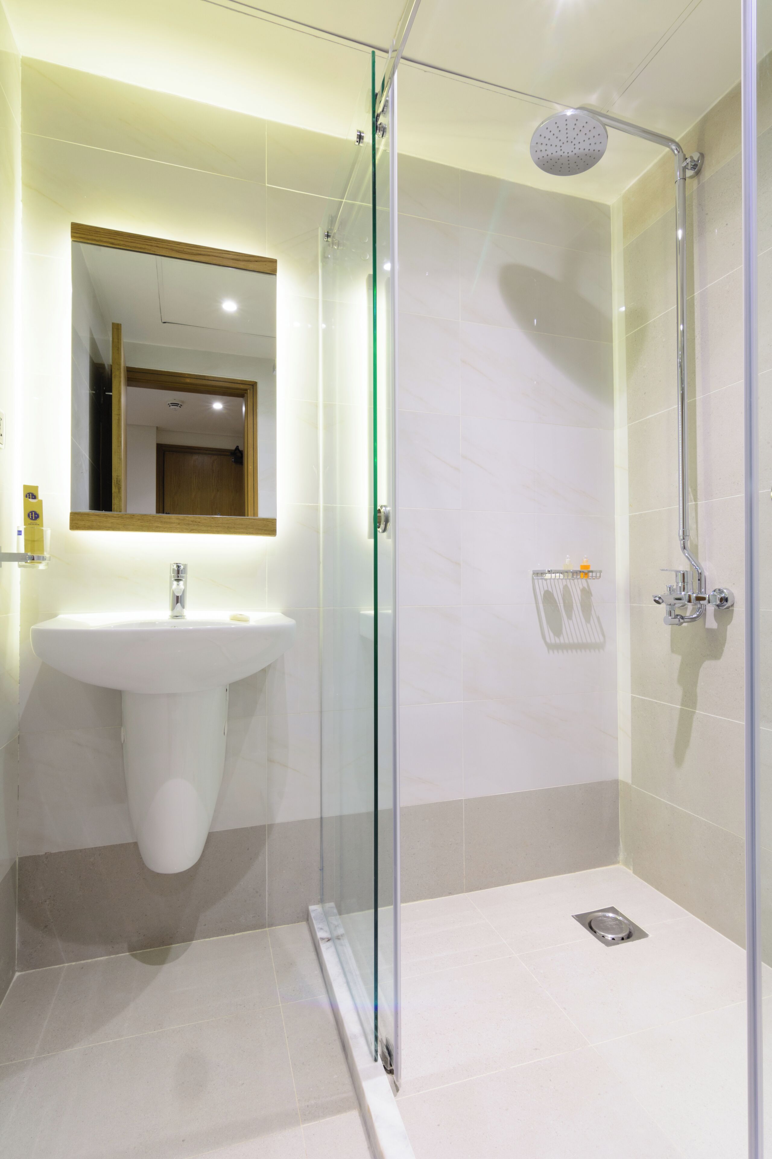 Ein modernes Badezimmer mit einer ein Glasfach werenden Dusche, einem weißen Waschbecken und einem Spiegel mit Holzrahmen.