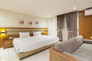 Una habitación de hotel con una cama grande, mesitas de noche, un sofá y un aire acondicionado instalado en la pared.