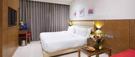 A hotel room with a large bed, a desk with a vase of flowers, a red sofa, and a TV on a wooden cabinet.